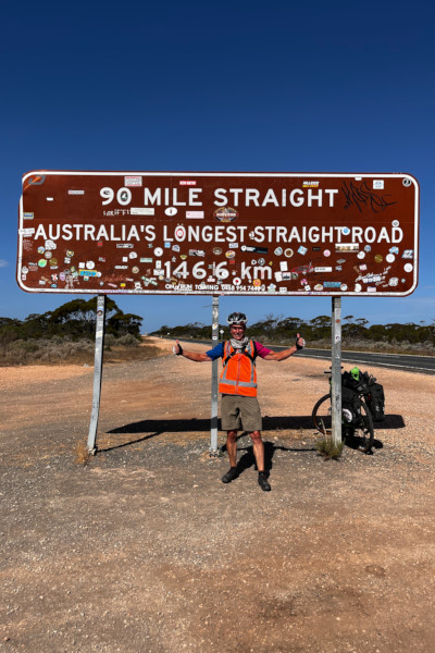 Mark smiling with his bike under a sign saying Australia's longest road