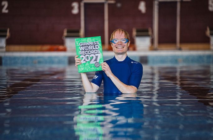 Christian in a swimming pool holding a Guinness World Records 2027 book