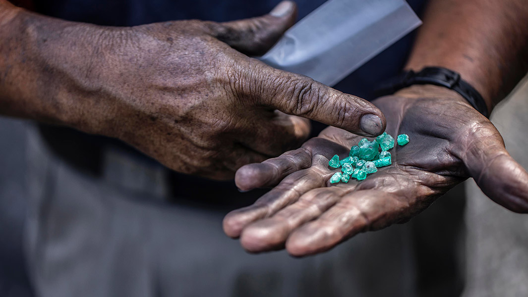 Split image showing a polished emerald gemstone set in a diamond-framed ring beside a rough emerald crystal in its natural rock matrix