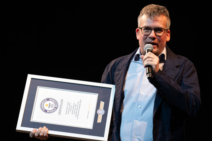 John speaking onstage and holding his GWR certificate