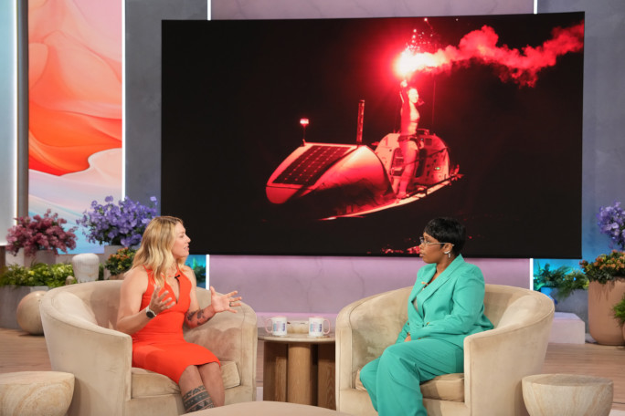 Kelsey and Jennifer Hudson talking with a photo of Kelsey rowing at night behind them