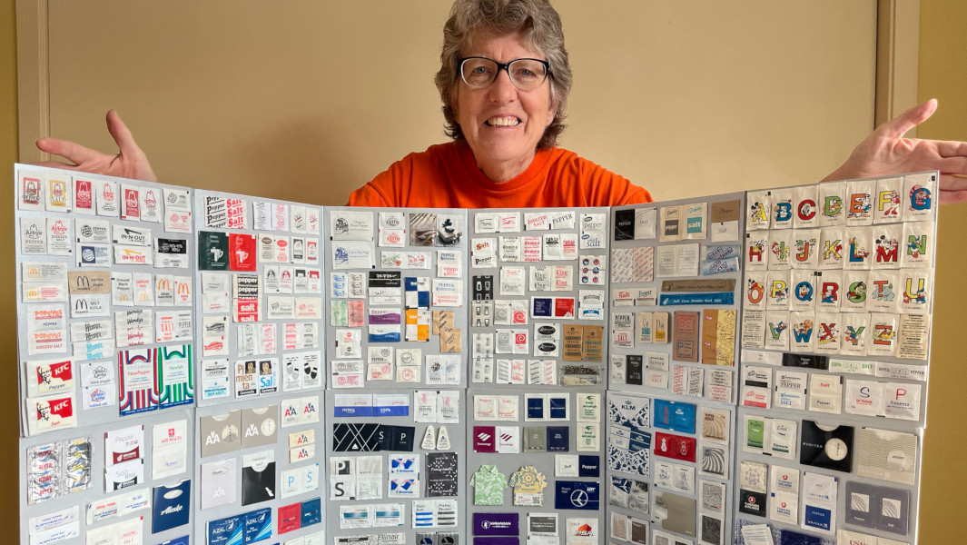 Linda Schulz smiling and showing off all her salt and pepper sachets displayed on a board