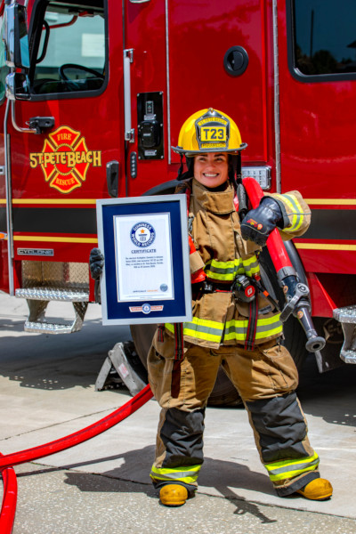 Autumn in her firefighter uniform, holding her certificate and hose, next to the firetruck