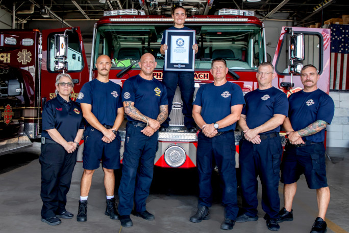 Autumn standing on the firetruck, holding her certificate, with her crew