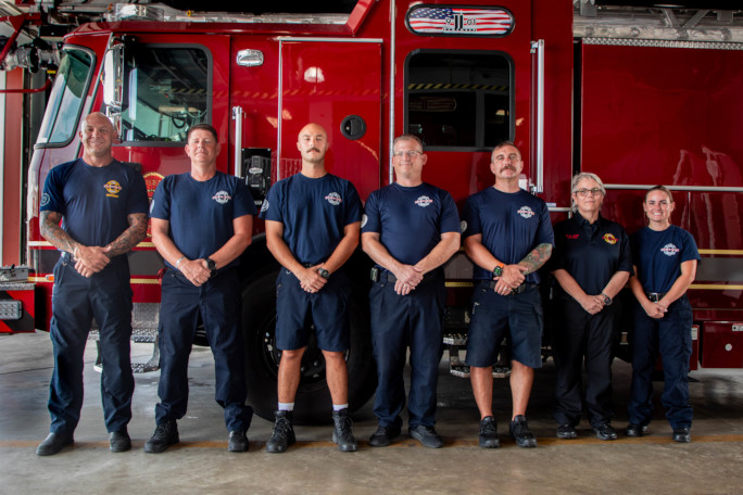 The crew and Autumn, all lined up by height in descending order, next to the firetruck