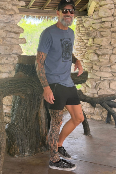 Scott smiling and standing while showing off his tattoos