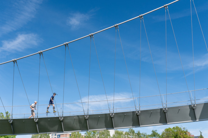 Jonathan crossing a bridge on his stilts, next to a man