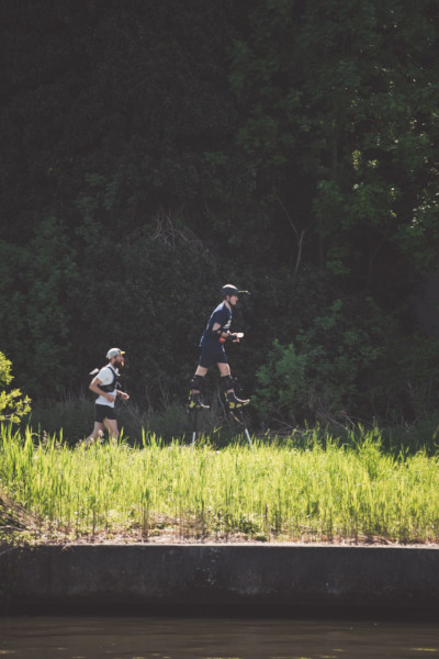 A far shot of Jonathan running next to a man near a grassy hill during the marathon