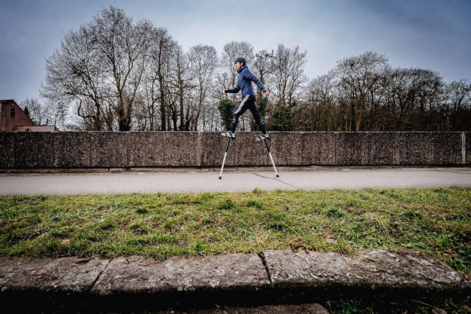 Jonathan walking on stilts near a grassy path by the canal
