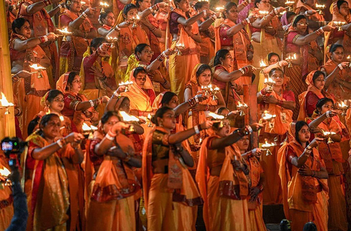 various people dressed in orange traditional wear rotate diyas