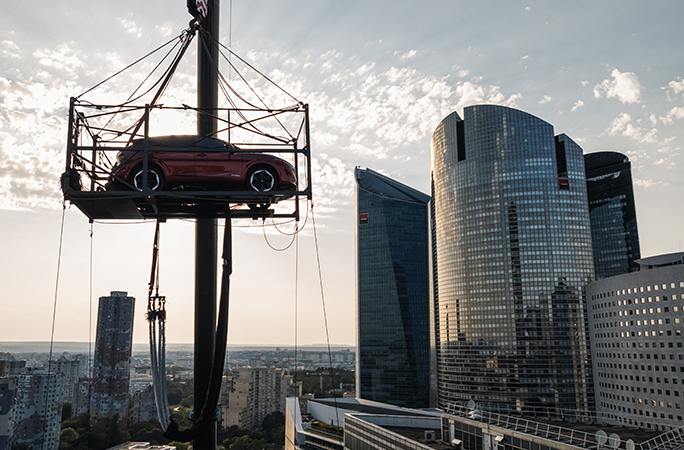 a-red-nissan-car-stays-stationary-in-a-cage-high-in-the-sky-supported-by-a-crane