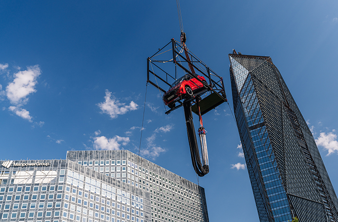 red Nissan car faces downwards on a platform held on a crane