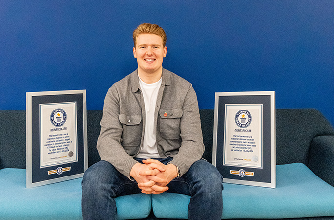 a man sits on a sofa with two guinness world records certificates