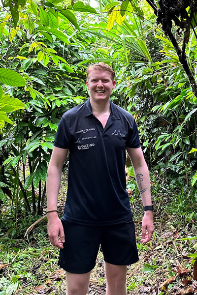 a man wearing a dark coloured t-shirt stands in the middle of the rainforest