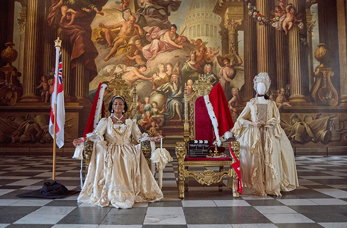 a woman dressed in a gold from the series bridgeton sits in a grand room