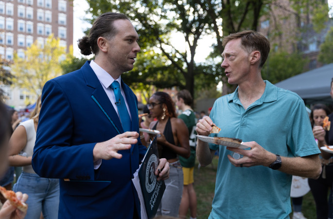 Thomas talking to a man eating a slice