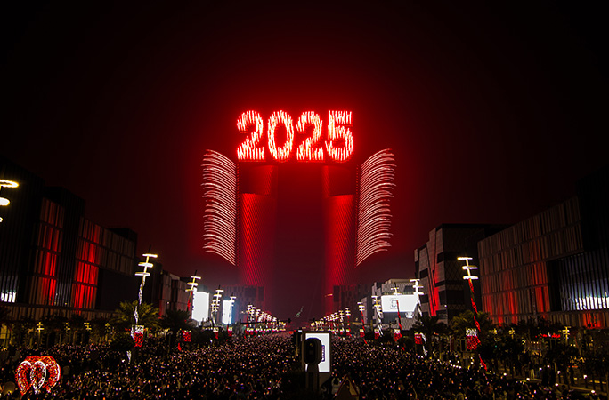 red fireworks spell out 2025 on the backdrop of city lights