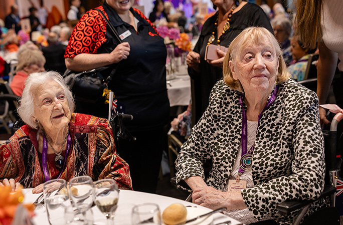 two elderly women sit in front of a dress table and look out in the distance