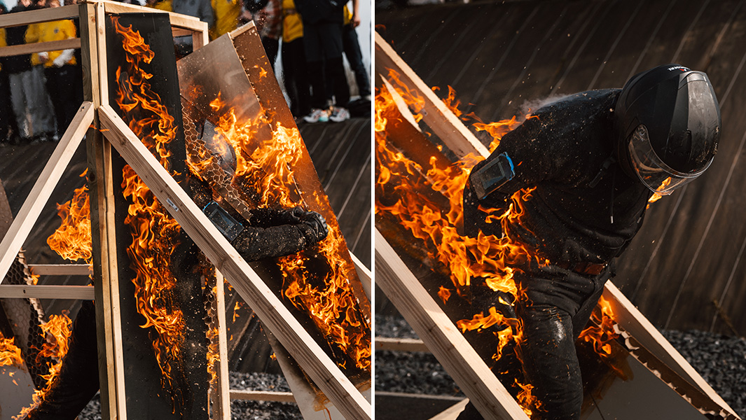 a man wearing a helmet runs through flaming doors while set on fire