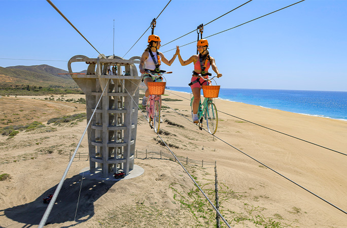 Girls high-fiving on the longest bicycle zip wire