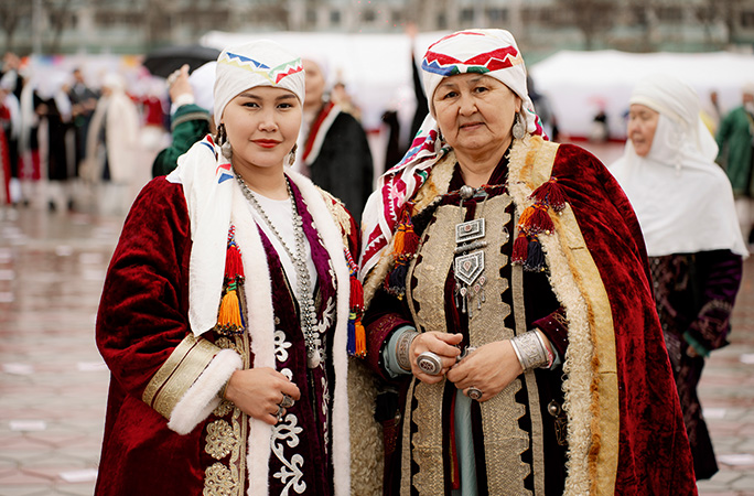 two women dressed up in traditional Kazakh clothing featuring red white and yellow notes