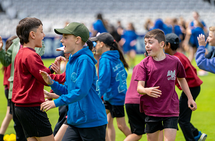 a group of children run around on green cricket grounds