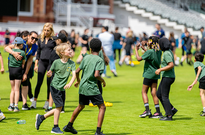 school children in green t shirts run around on cricket grounds