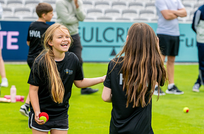 two children smiling at each other with a cricket ball in hand