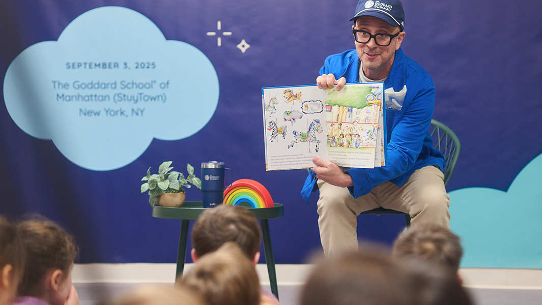 a man wearing a blue hoodie and blue cap reads a book to children