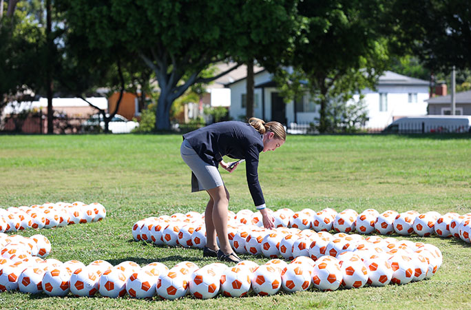 a woman dressed in a guinness world records adjudicator uniform count soccer balls on the grass
