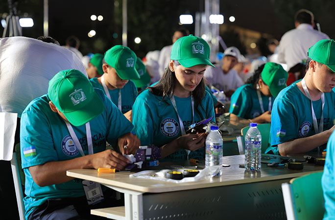a row of students dressed in blue start assembling robots