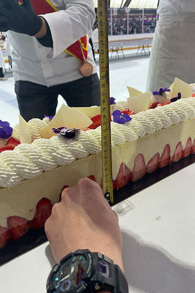 a hand takes a ruler to the longest strawberry cake to measure it