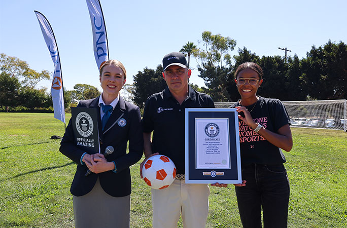 two women stand beside a man smiling holding a guinness world records certificate