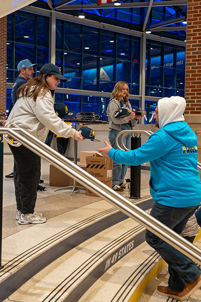 a woman dressed in a grey hoodie passes out a blue hat