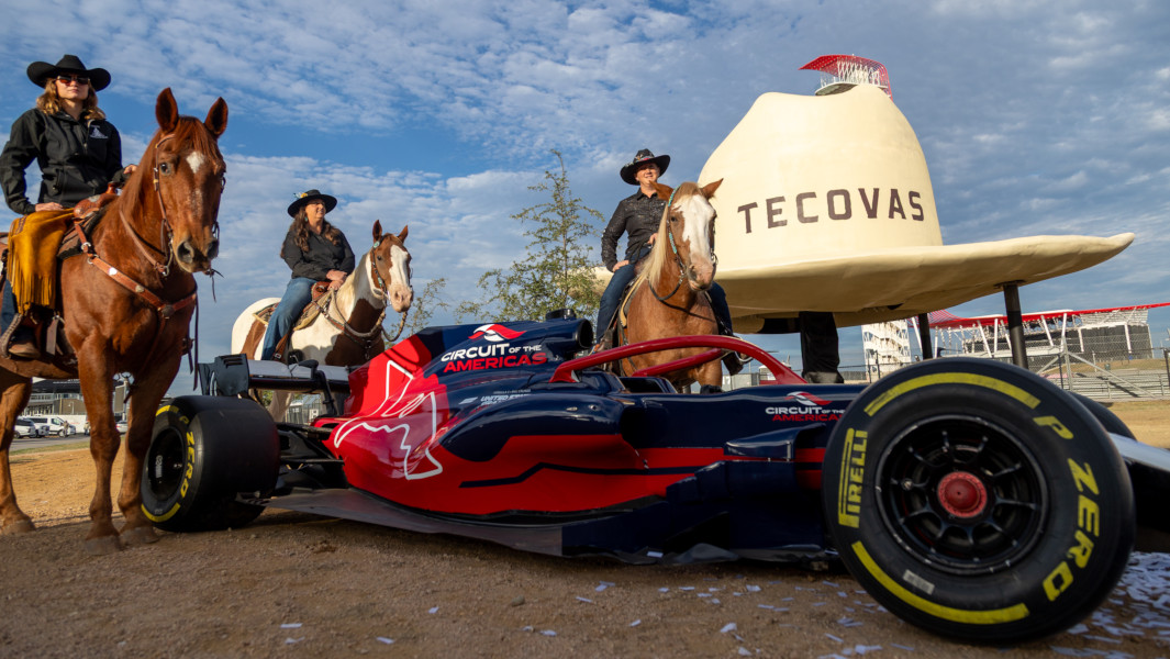 Cowboys standing next to a racecar with the largest cowboy hat sculpture behind them