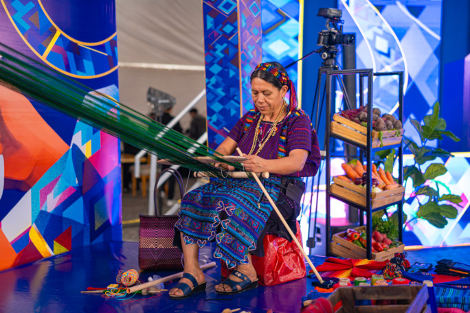 A woman in traditional Guatemalan clothing weaving onstage