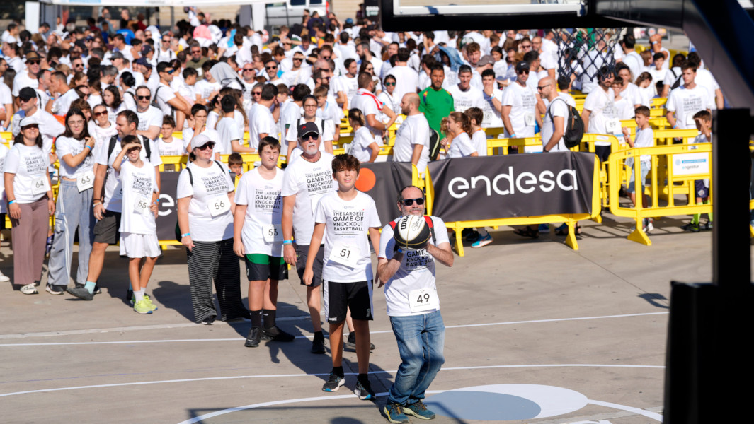 A man shooting a basket at the knockout game, with a giant line of people behind him