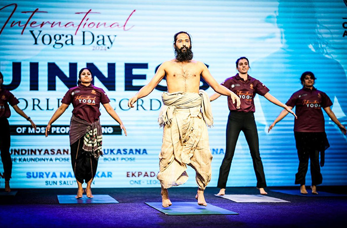 a shirtless man with a beard instructs a yoga class