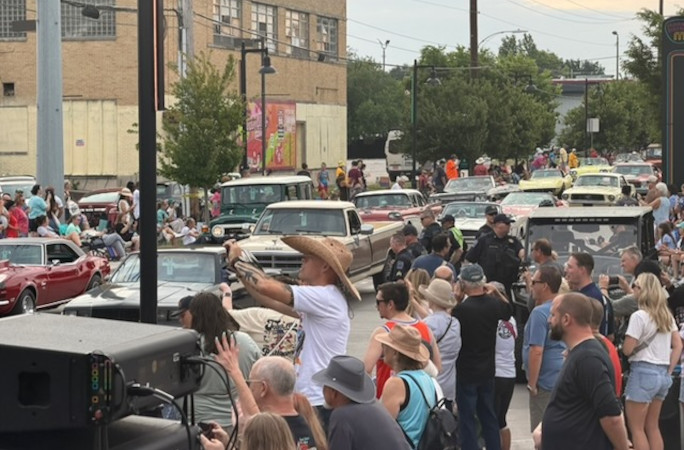 Multiple cars going in the parade while surrounded by the crowd
