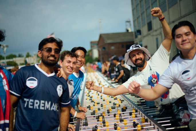 Four men smiling around the longest foosball table