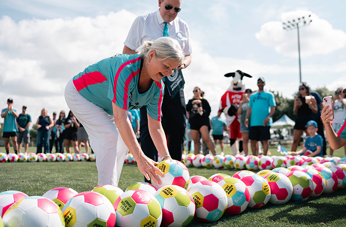 a blond woman adds a soccer ball into a row of soccer balls