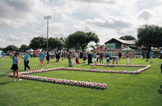 group of people line soccer balls to resemble the number two