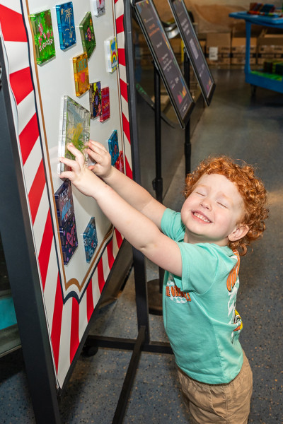 A kid smiling as he places a MAGNA-TILE onto the mosaic