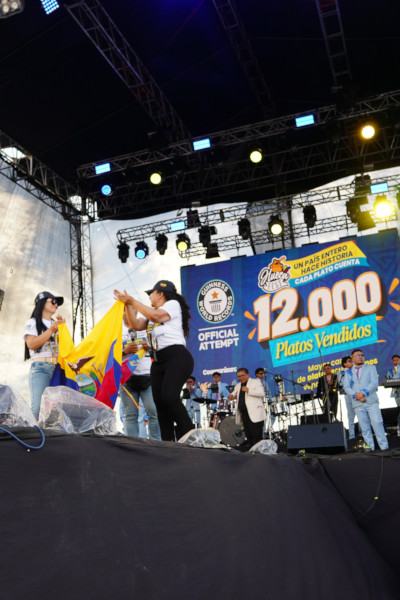 Two organizers celebrating onstage as the announce they've sold 12,000 plates