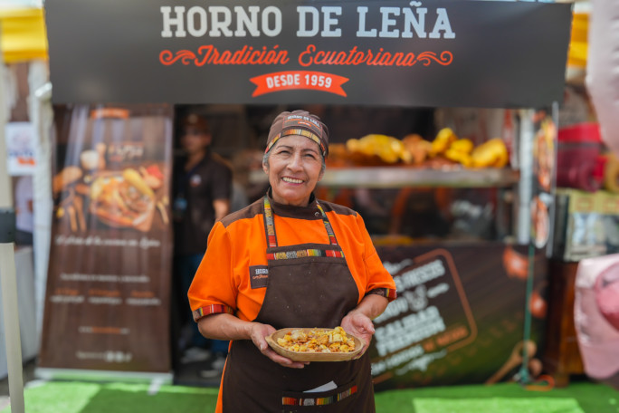 A woman smiling and holding food outside her stall