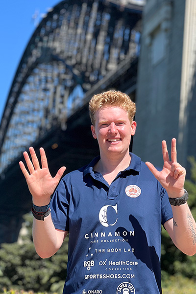 man puts his fingers up in an eight formation in front of a bridge