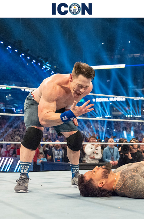 John Cena leaning over defeated opponent. His hands are in front of his face as he is doing his 'You cant see me' pose.