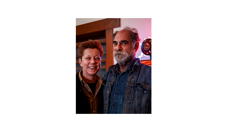 Dydia DeLyser and Paul Greenstein standing in front of neon light